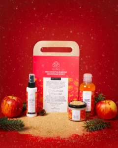 Luxury body care gift set placed on a bed of brown sugar, with a festive red Christmas background and falling snow, professional hero shot